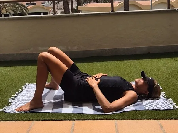 Emma lying on her back on a mat, knees bent, tennis balls under her sacrum